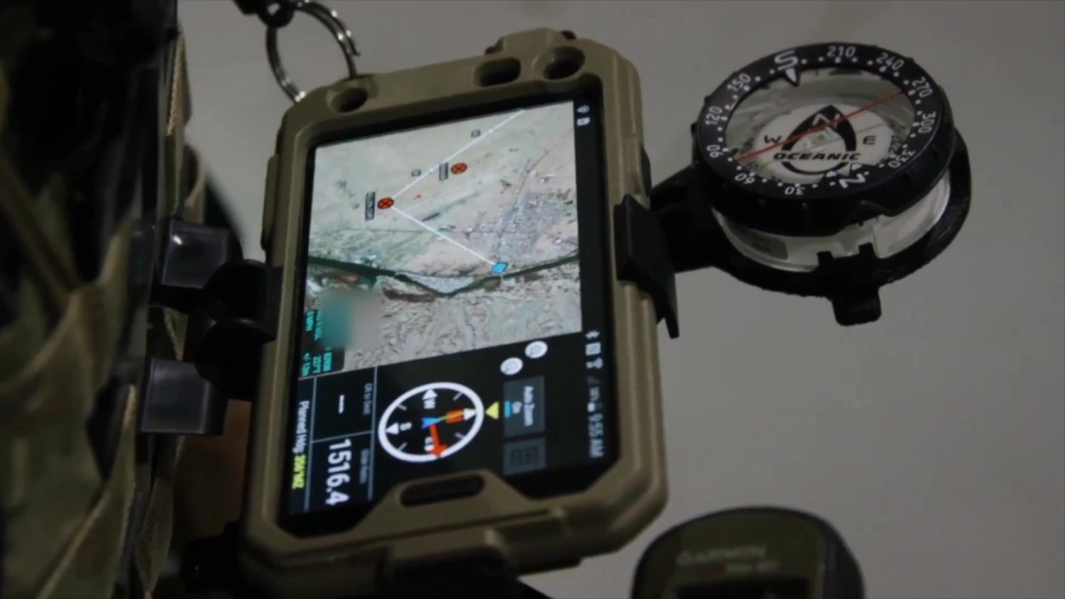 Rugged-cased end-user device mounted on a plate carrier running a tactical map with heading and grid readout, magnetic compass alongside
