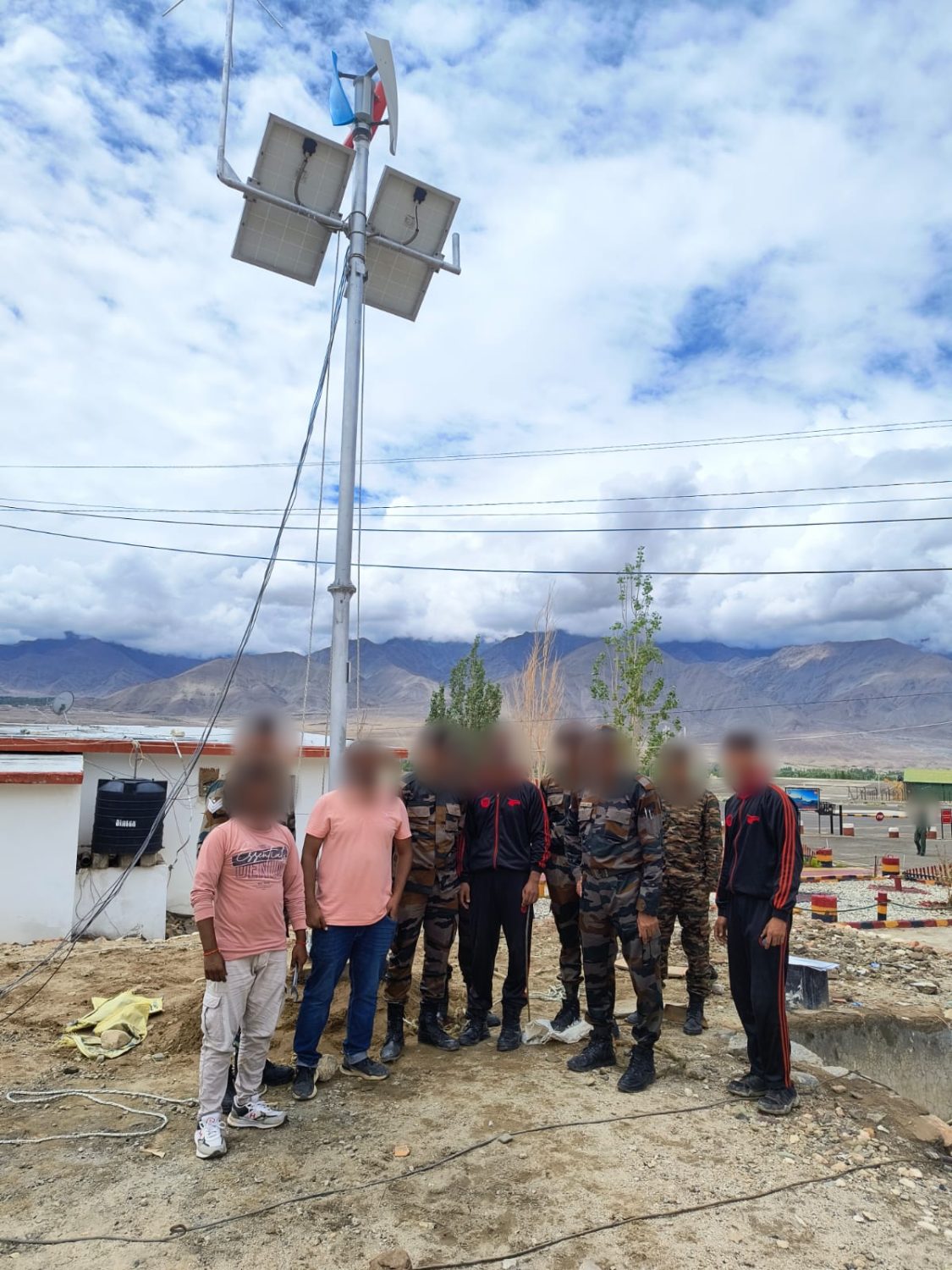 Mast with solar panels and a vertical-axis wind turbine installed at a high-altitude site, team alongside